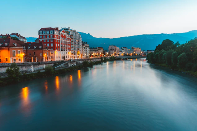 A serene riverside lodge at sunset, glowing warmly amidst Bhutan’s tranquil mountains.