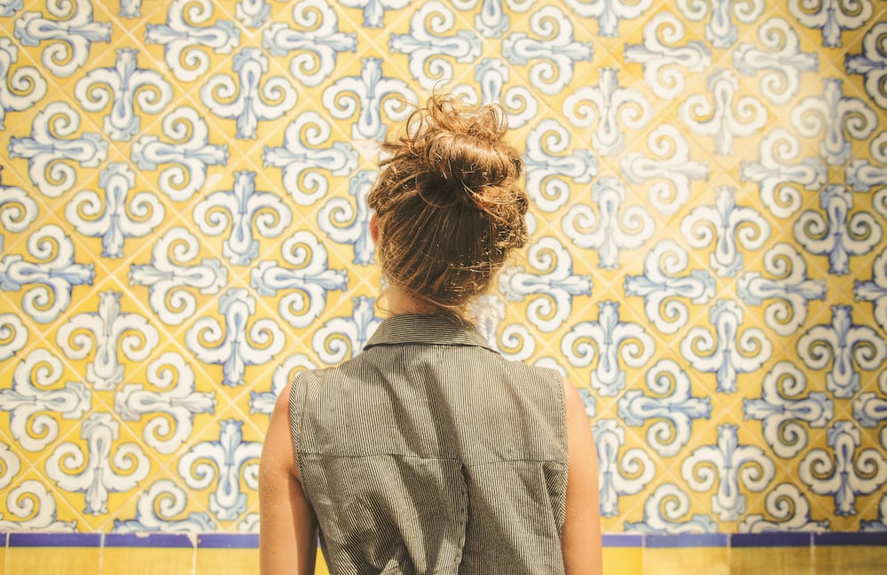 woman in gray collared sleeveless top facing white and yellow floral wall