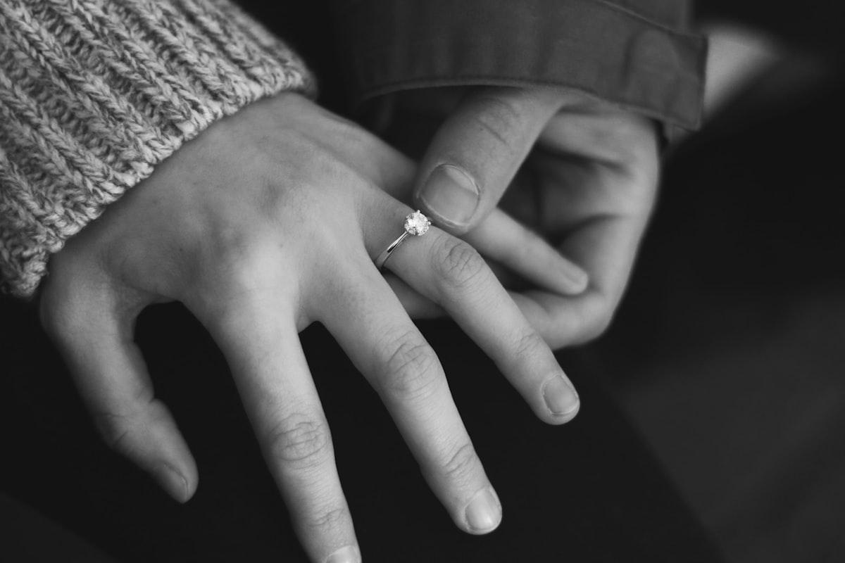 The hands of a couple showing off the engagement ring, black & white photo. 
