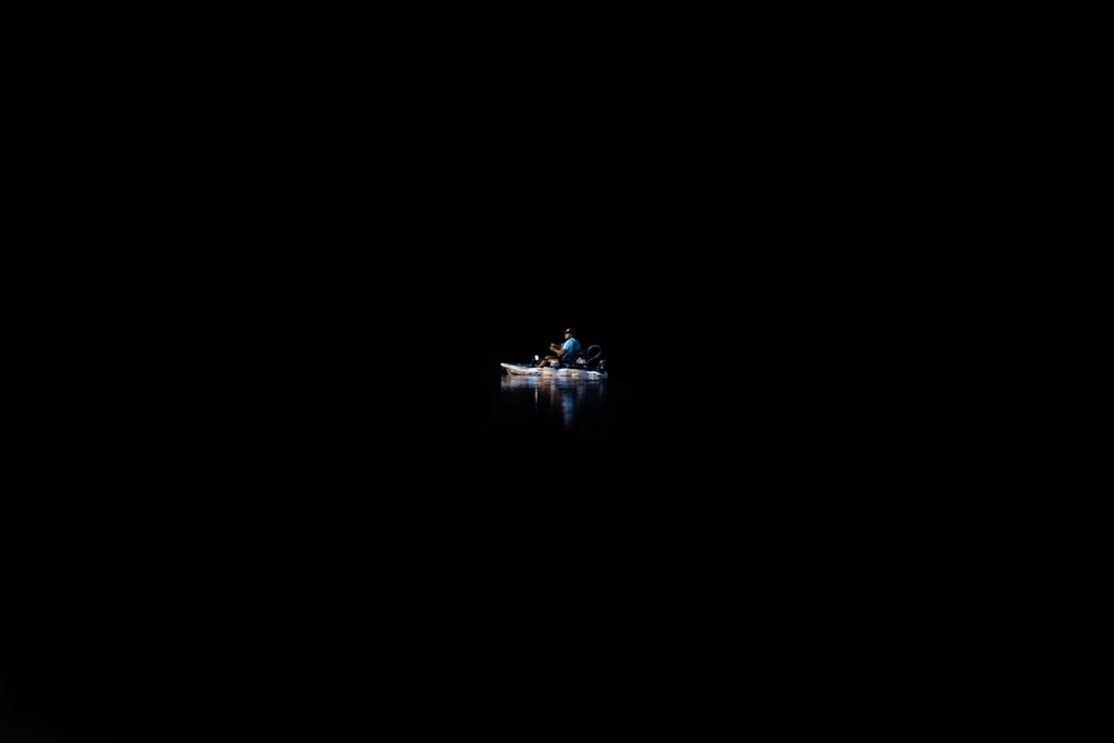 A person on a canoe in the water surrounded by complete darkness.