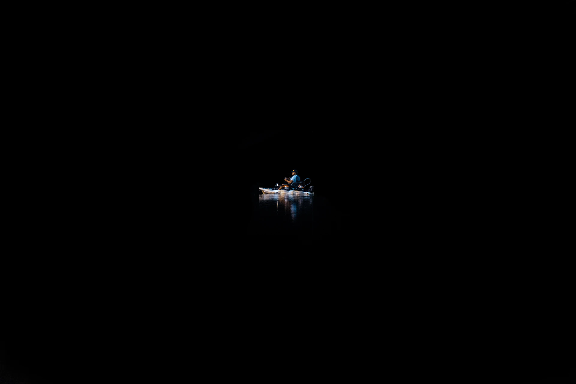 A person on a canoe in the water surrounded by complete darkness.