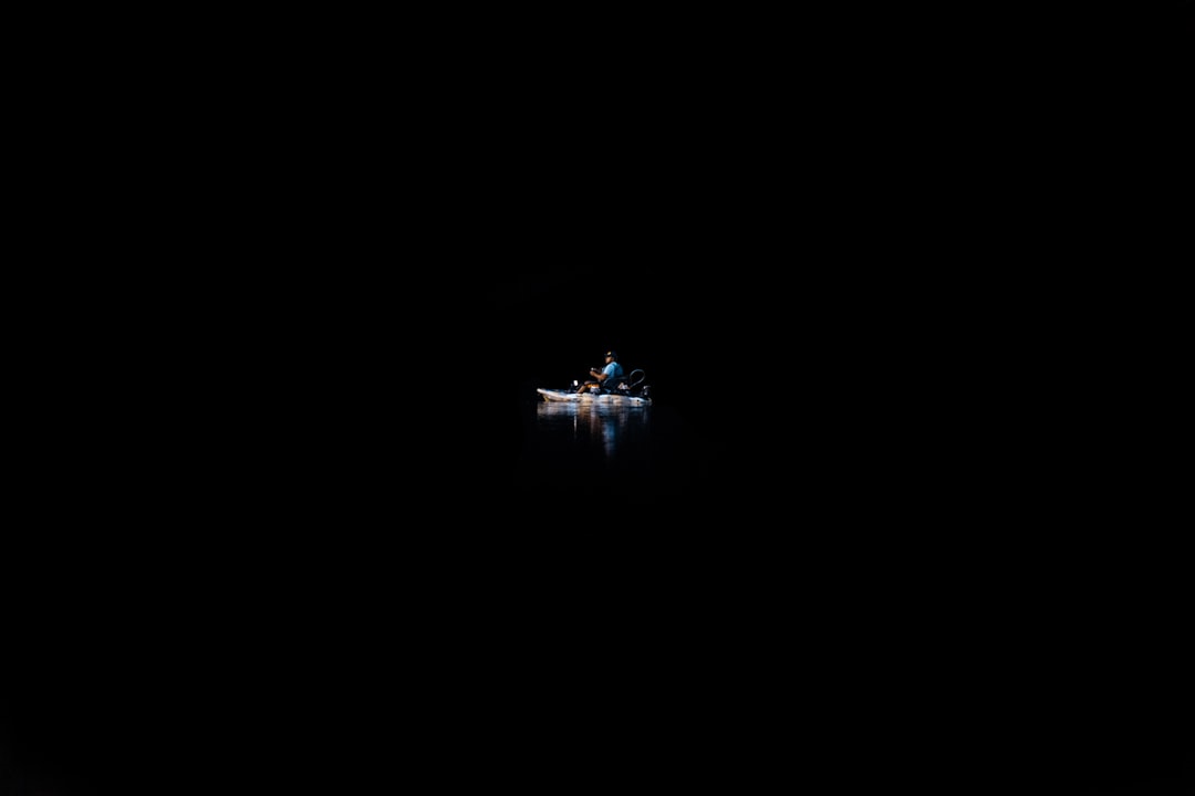 A person on a canoe in the water surrounded by complete darkness.