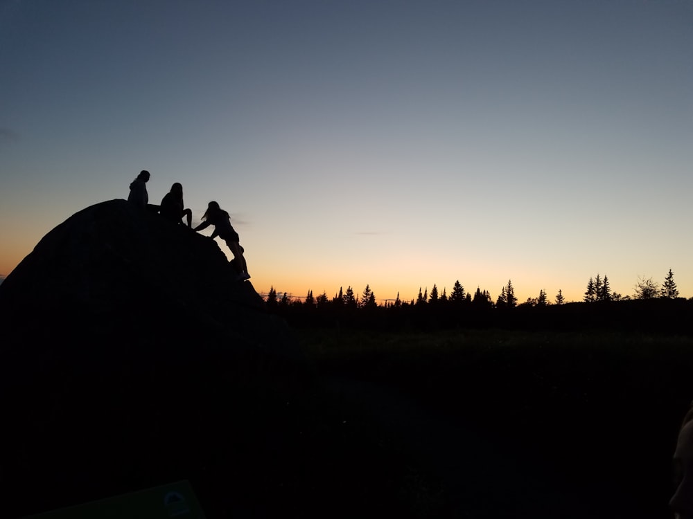 silhouette of three people on hill near trees during sunset