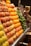 A market stall neatly displays rows of fresh fruits including peaches, oranges, and grapes, alongside green peppers. The produce is organized in sections, showcasing vibrant colors and inviting freshness.