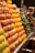 A market stall neatly displays rows of fresh fruits including peaches, oranges, and grapes, alongside green peppers. The produce is organized in sections, showcasing vibrant colors and inviting freshness.