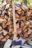 A rugged axe with a freshly sharpened edge resting against a stack of firewood outdoors.