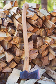 A rustic axe leaning against a stack of firewood outdoors.