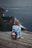 woman sitting on brown plank facing body of water