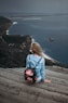 woman sitting on brown plank facing body of water