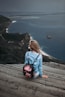 woman sitting on brown plank facing body of water