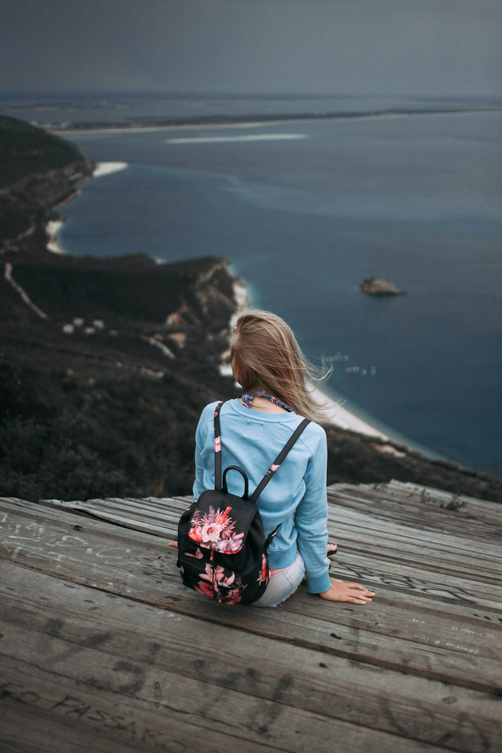 woman sitting on brown plank facing body of water