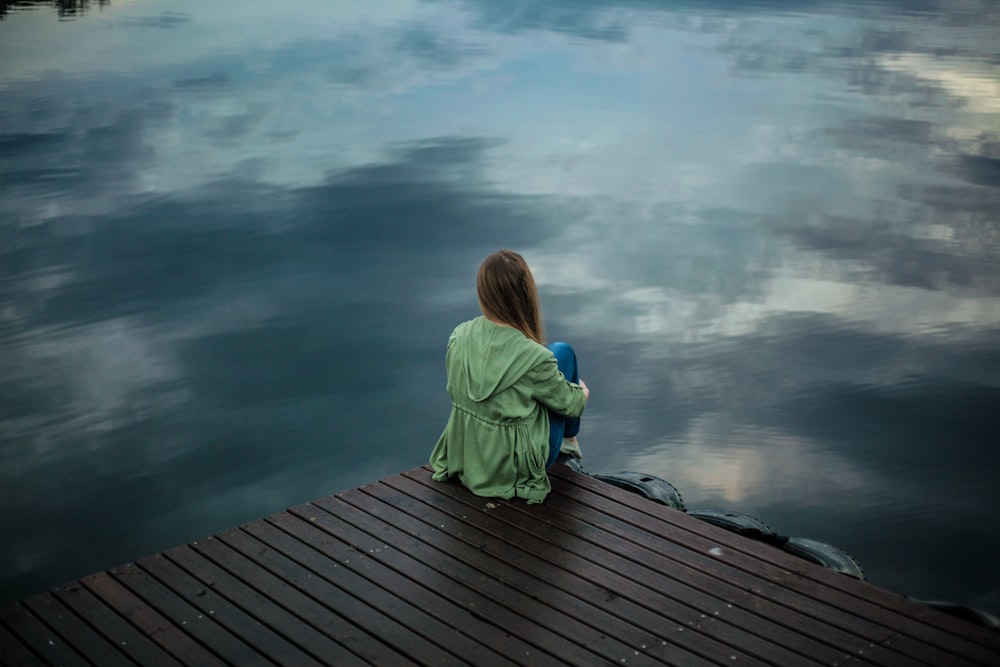 woman sitting on dock near body of water