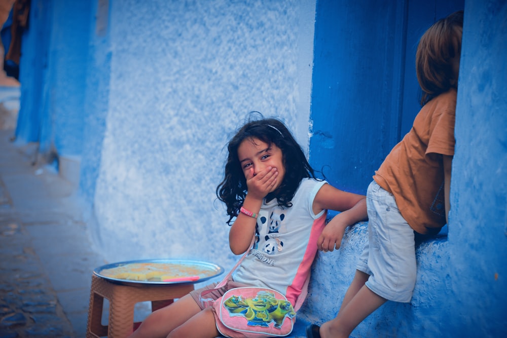 deux enfants appuyés sur le mur bleu