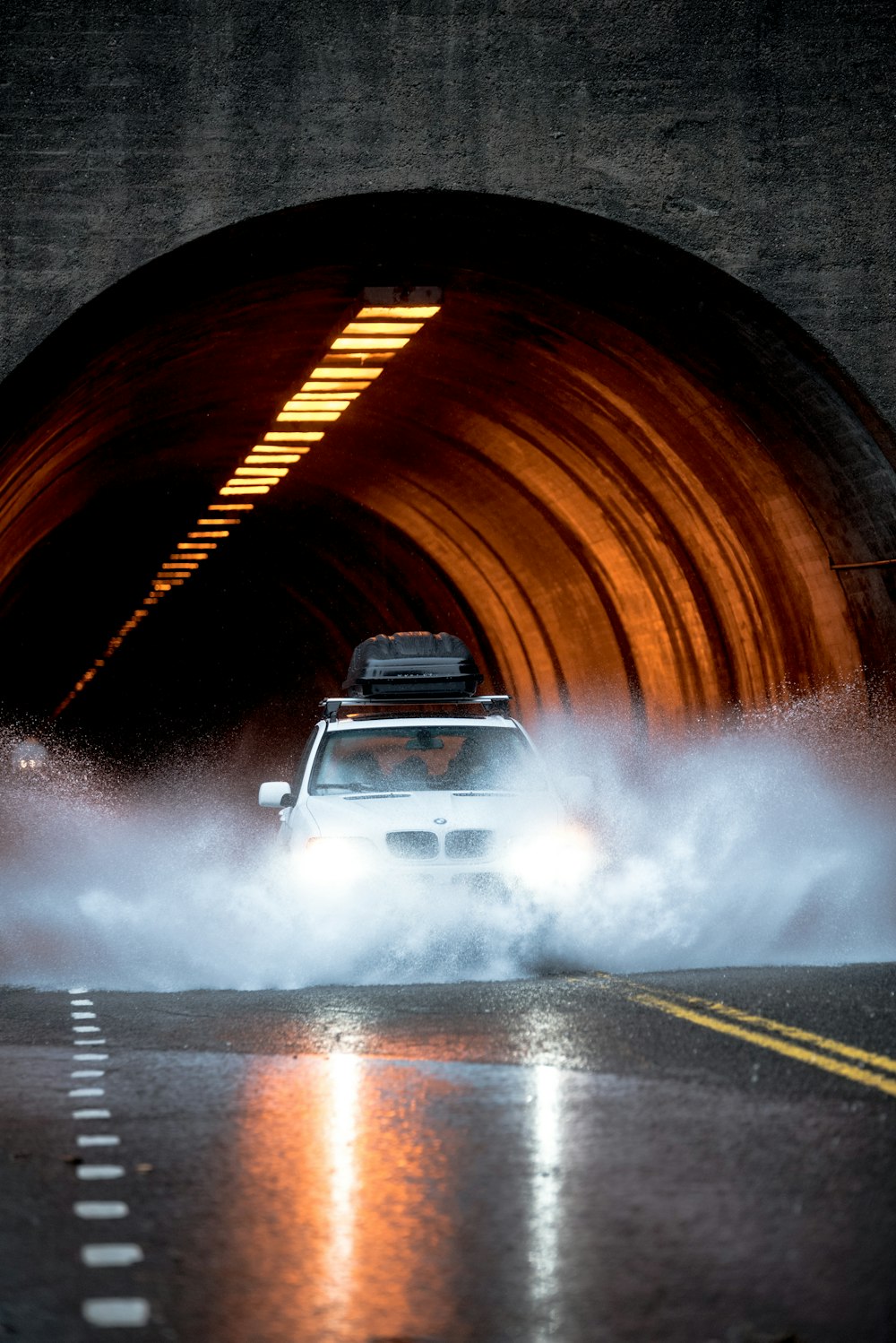 carro BMW branco atravessando estrada de asfalto em frente ao túnel de concreto