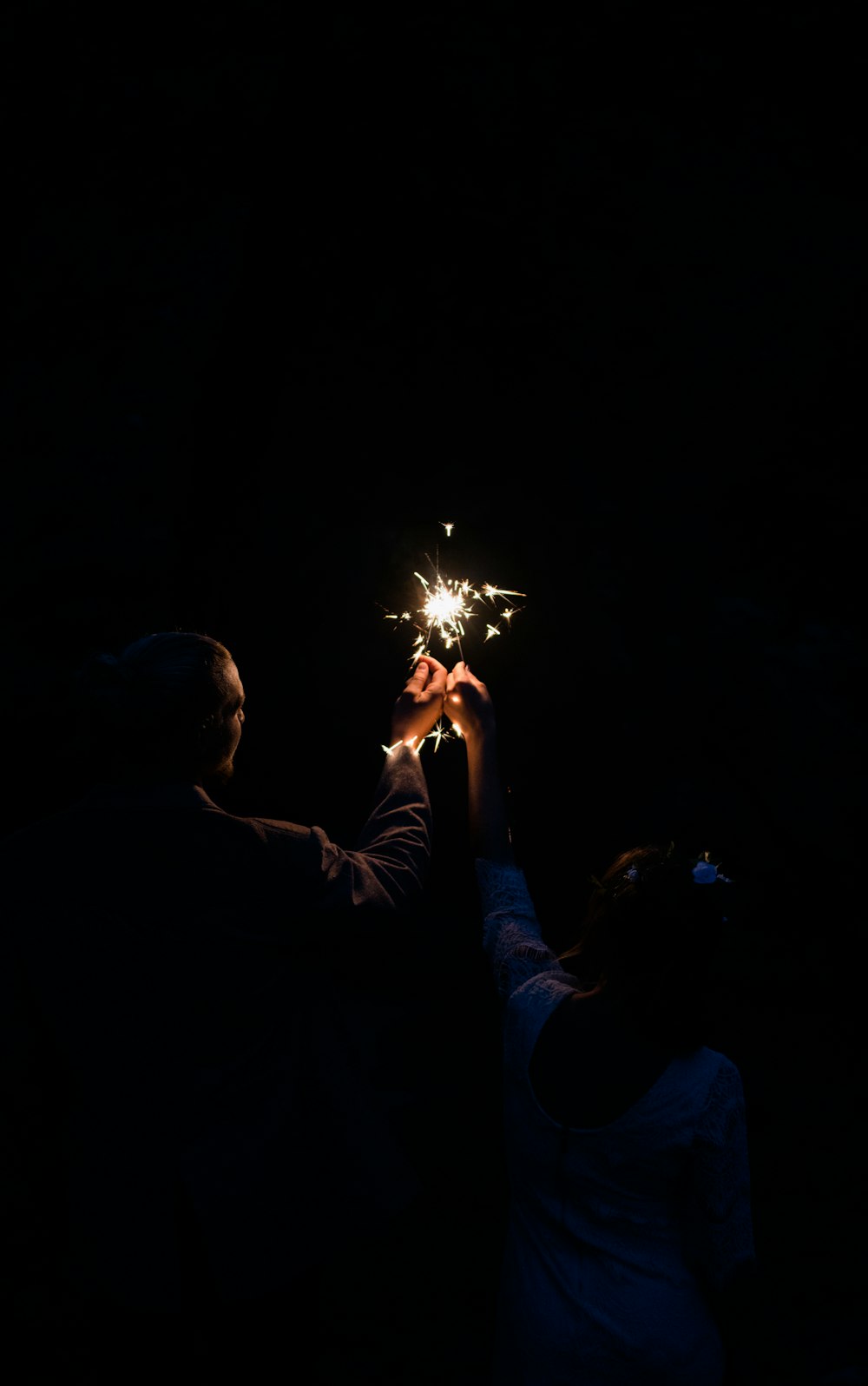 man and woman holding firecracker at nighttime