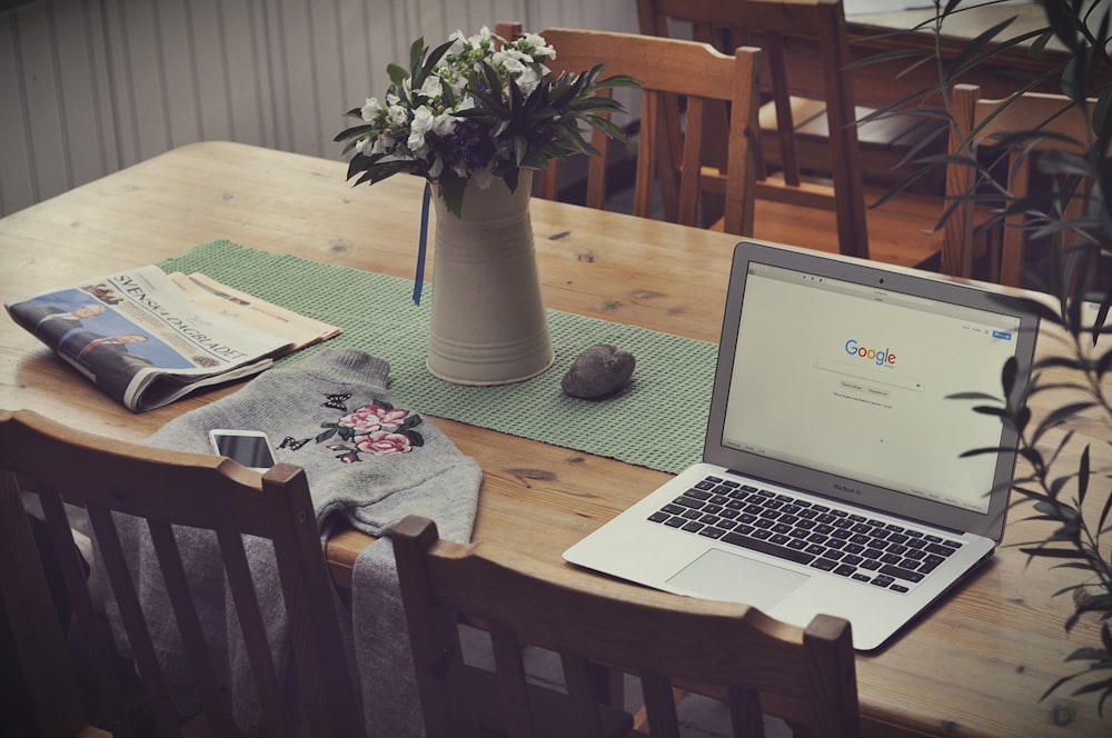 laptop em cima da mesa ao lado do vaso de flores