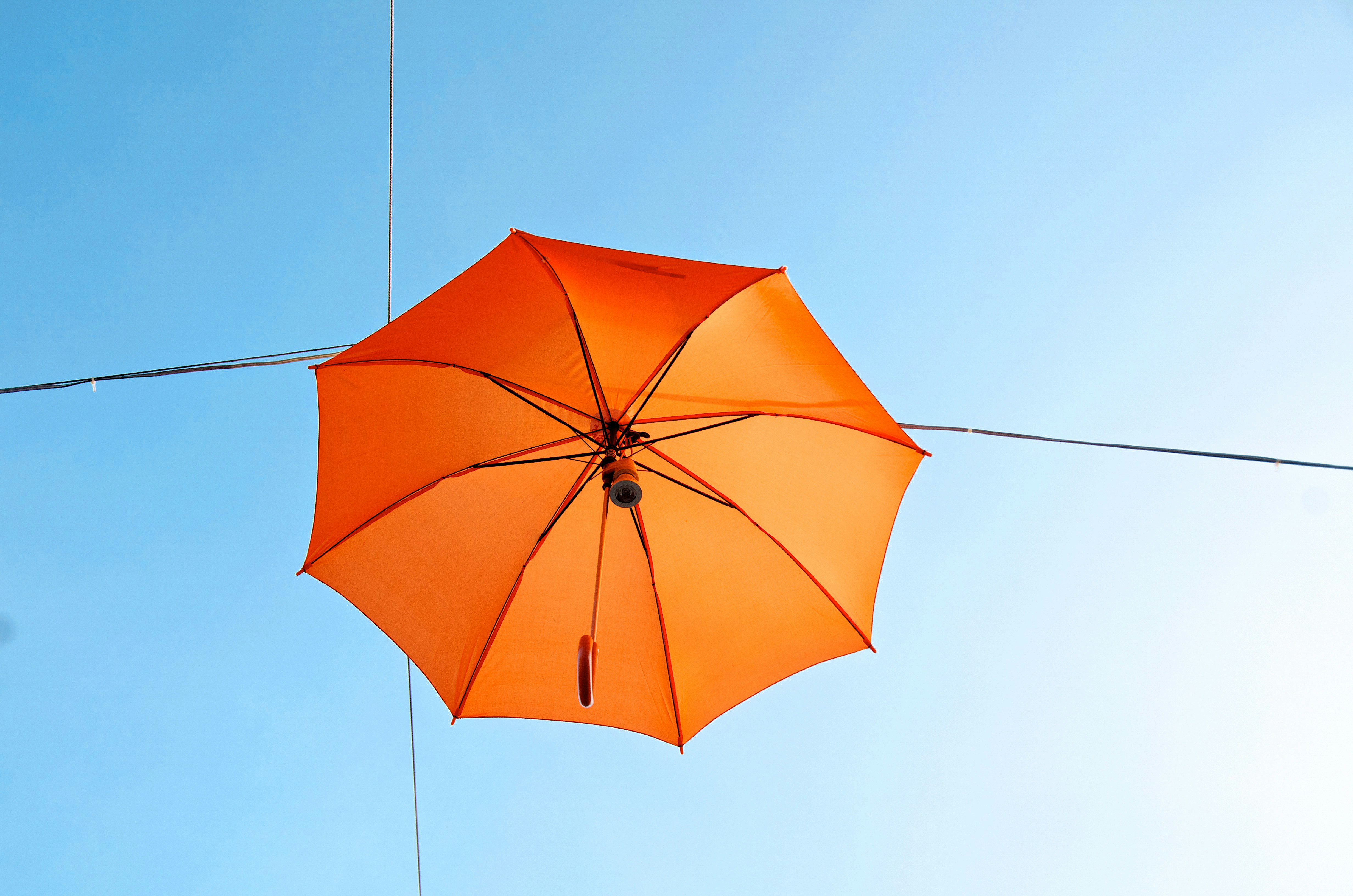 an orange umbrella hanging from a wire against a blue sky, party preparation (-)