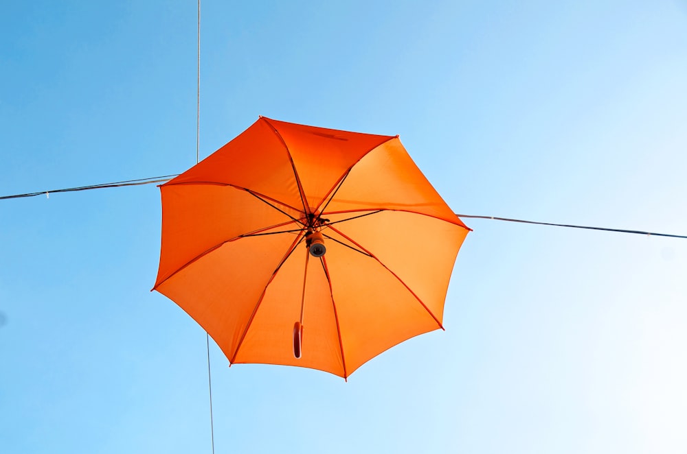 an orange umbrella hanging from a wire against a blue sky