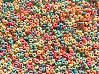 A close-up view of a large number of colorful, ring-shaped breakfast cereals. The rings are brightly colored in red, orange, yellow, green, and purple, creating a vivid and playful appearance.
