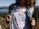 A person in a denim jacket is pulling it open to reveal a white t-shirt with text that reads 'RIGHT TO BE WRONG' and 'be free go your own way.' The background features a scenic view of a forest and a lake under a clear sky.
