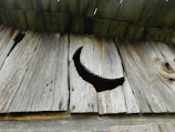 Weathered wooden boards are arranged vertically, with a crescent-shaped cutout in one of the planks, allowing light to pass through. The wood appears aged, with visible grain and knots.