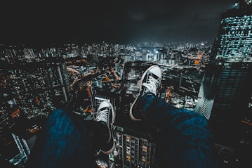 person wearing converse sneakers and blue jeans facing nyc cityscape during nighttime