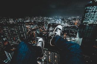 person wearing blue jeans facing cityscape during nighttime