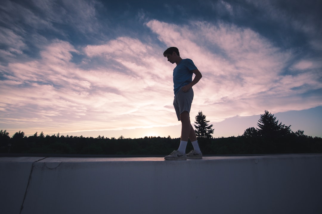 man standing on white concrete ledge below cloudy sky during dawn