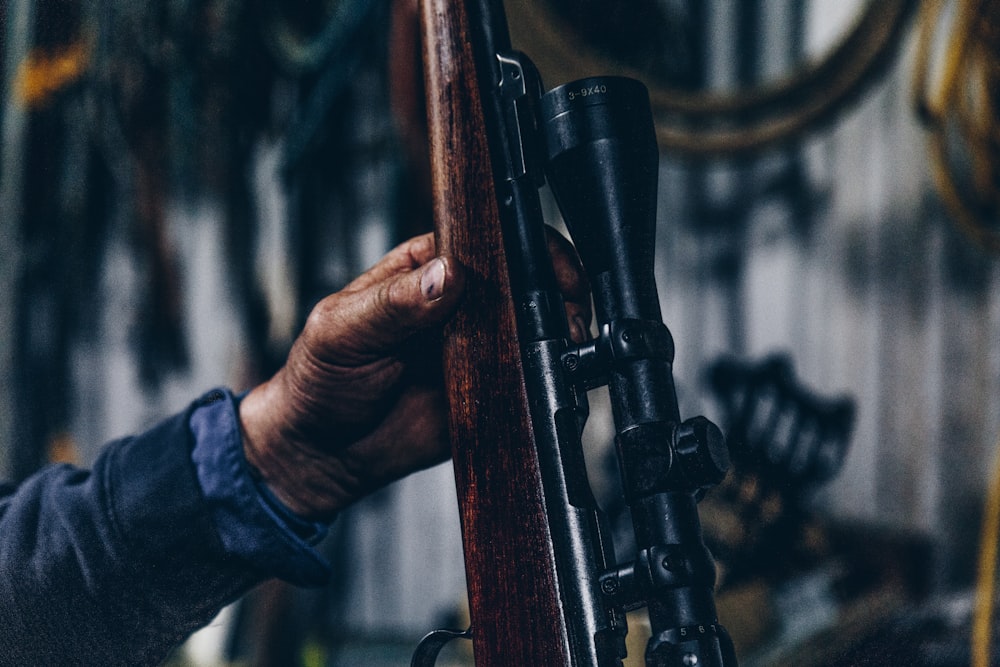 Persona que sostiene un rifle de caza marrón y negro