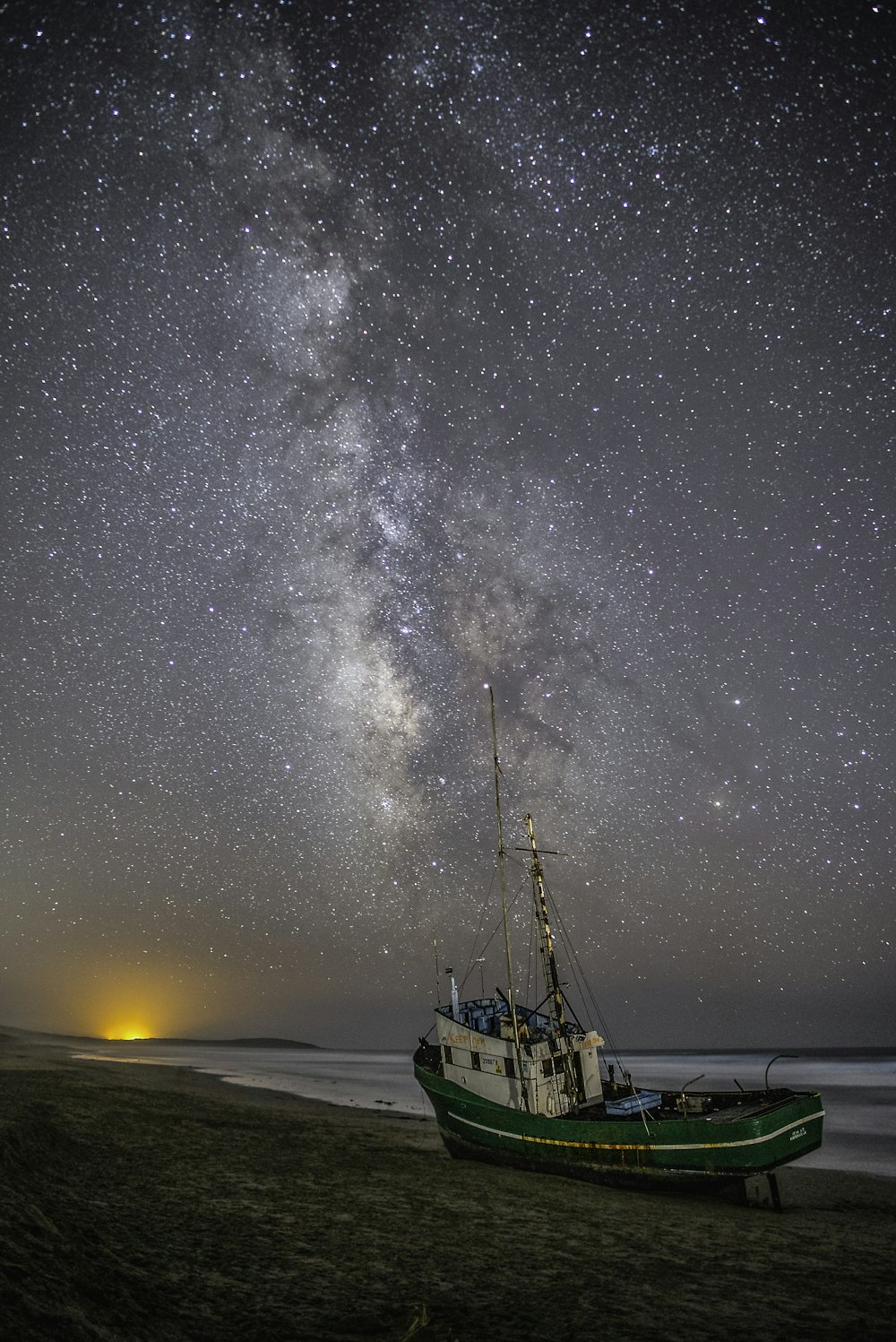 green and white fishing boat on gray sand under white and gray sky