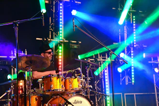 Klutch passionately playing drums on stage, surrounded by warm stage lights and an engaged audience.