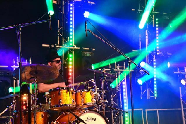 Klutch passionately playing drums on stage, surrounded by warm stage lights and an engaged audience.