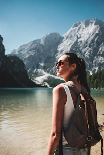 photo of woman wearing white tank top and gray backpack standing near body of water