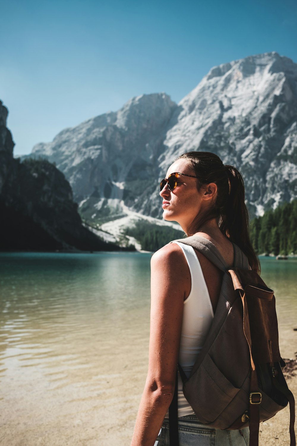 photo of woman wearing white tank top and gray backpack standing near body of water
