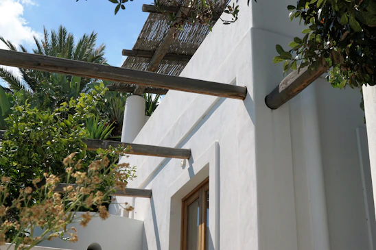 A clean, minimalist outdoor patio structure with modern lines, surrounded by lush greenery under soft natural light.