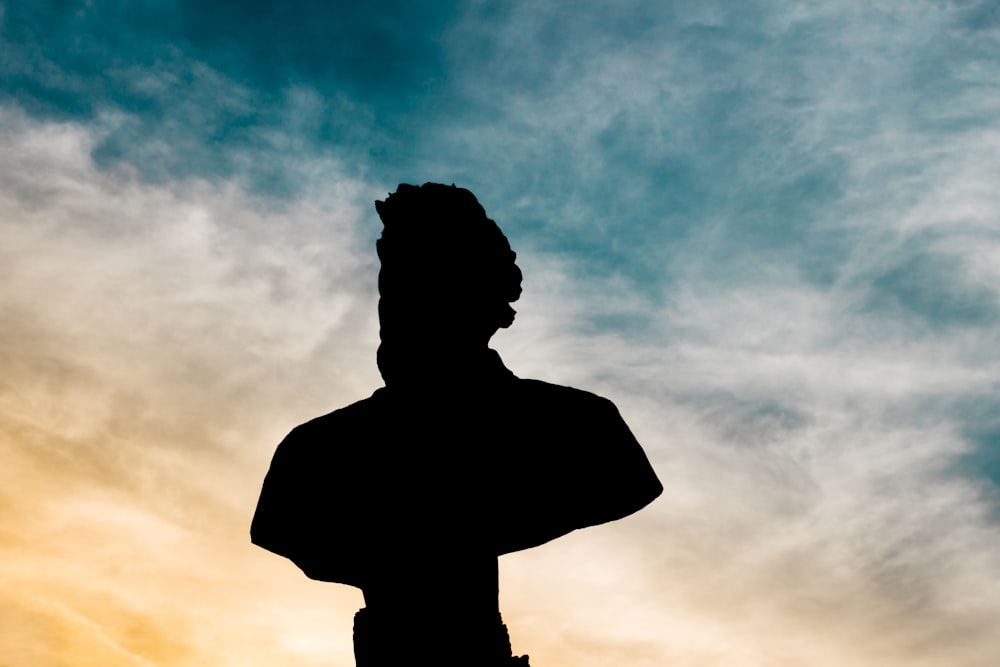 silhouette de statue buste d’homme sous le ciel nuageux pendant la journée