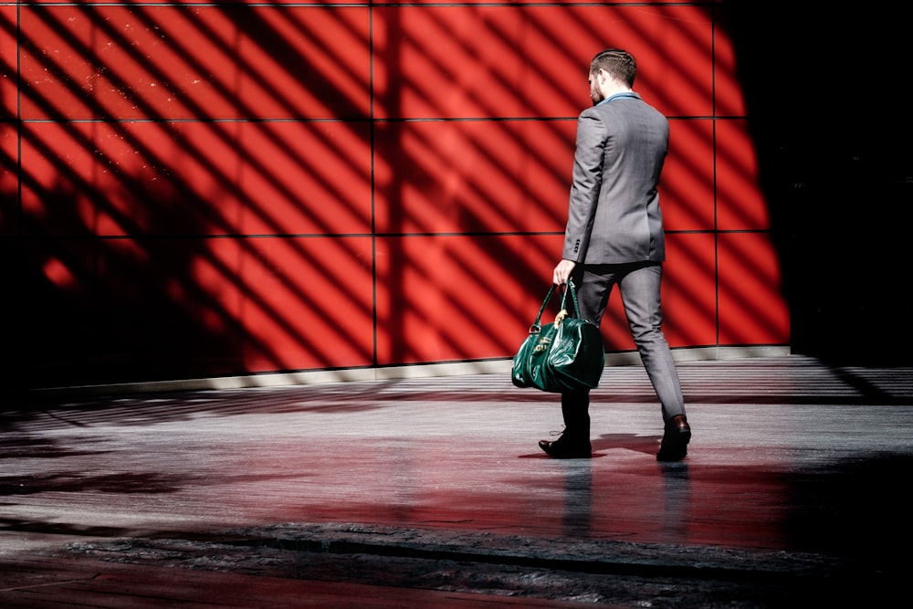 man holding green duffel bag while walking near red building at daytime