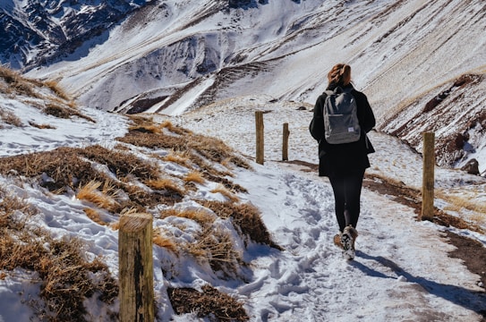 A traveler wearing layered warm clothing walking along a mountain trail with a backpack.