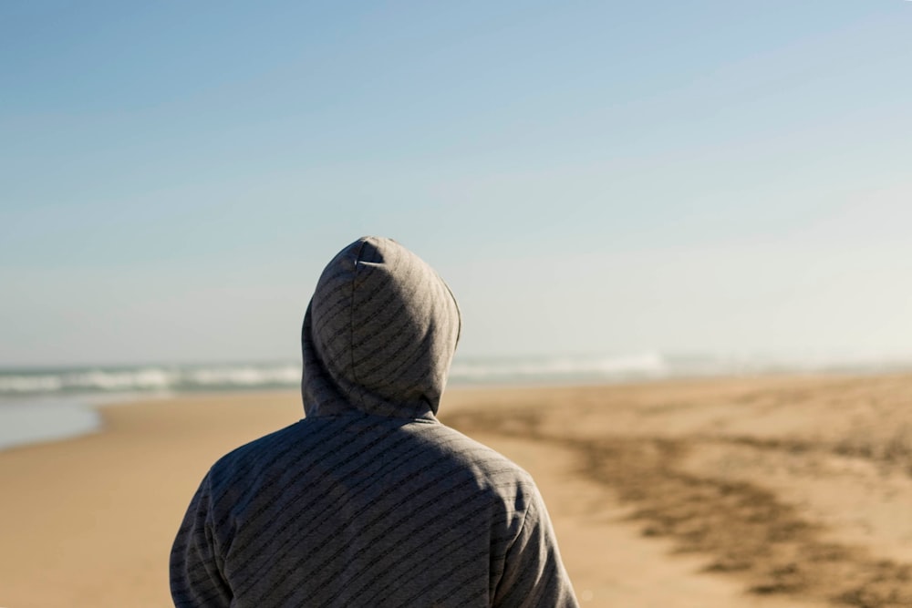 person wearing gray hooded top facing seashore