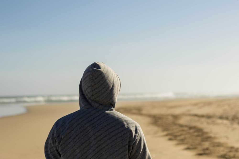 persona che indossa un top con cappuccio grigio rivolto verso la riva del mare
