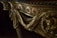 Intricately carved wooden detail of furniture featuring ornamental floral patterns and a sculpted animal figure. The design includes flowing drapery motifs and twisted column elements.