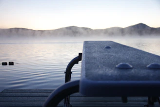 Serene lakeside dock with gentle ripples under a soft morning fog.