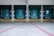 Five industrial loading dock doors painted in teal, lined side by side. Each door features small rectangular windows and is framed by black and yellow warning stripes. The concrete ground in front of the doors is marked with red lines.