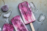 purple and white ice pop lying on wet ground with ice