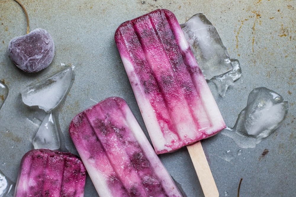 purple and white ice pop lying on wet ground with ice