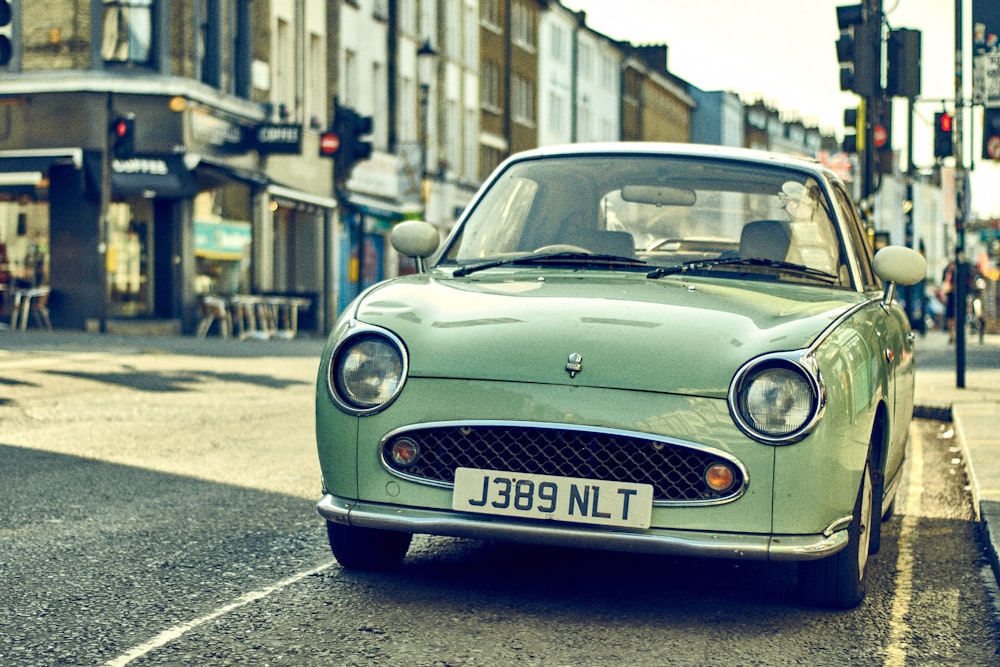 green car parked along the road in front of traffic lights near buildings