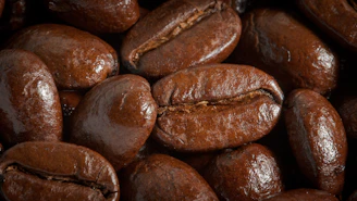 Close-up of glossy coffee beans with golden light reflections on a matte black surface.