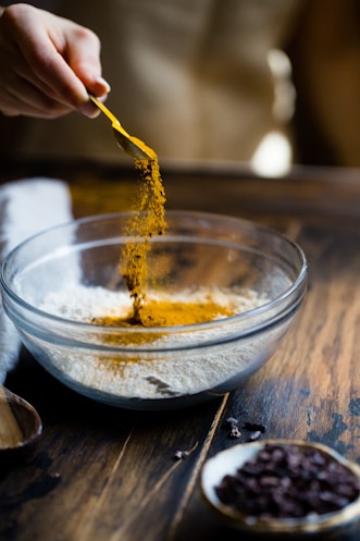 person pouring seasonings on clear glass bowl