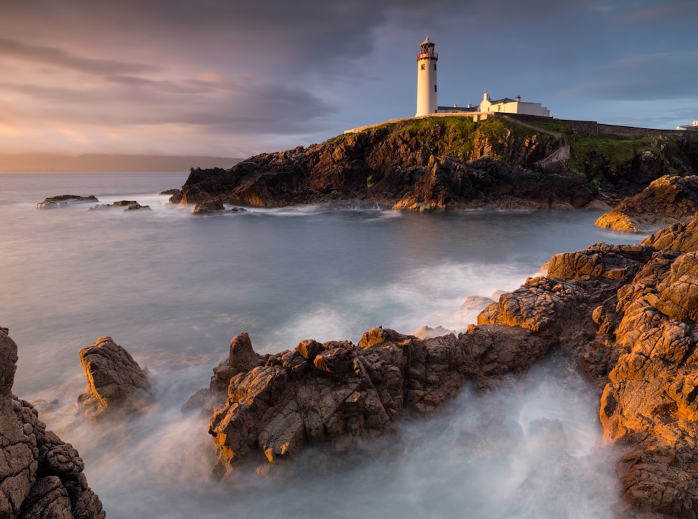 white lighthouse on hill during black clouds