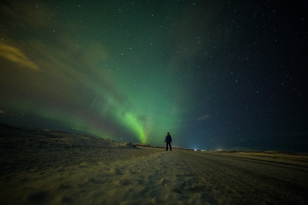 silhueta da pessoa em pé na areia marrom sob a aurora boreal